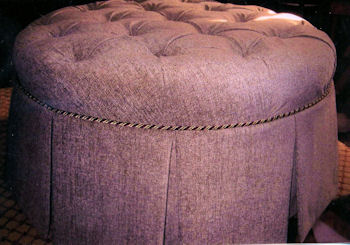 Pink colored ottoman covered in woven fabric with cord trim